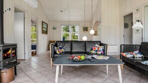 A cozy living room with a fireplace, a sofa, a coffee table with fruits and magazines, and a view of the outdoors. - "Hauke" - 478m from the sea by Interhome (Hjørring)