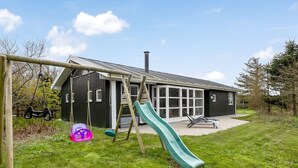 A playground with a slide and swings, a house with a dark exterior, and a clear sky. - "Hauke" - 478m from the sea by Interhome (Hjørring)