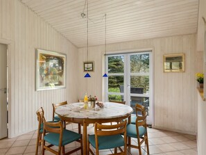 A dining area with a round table, wooden chairs, a blue pendant light, and a view through a glass door.
