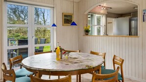 A dining area with a round table, chairs, and a view through large windows. - "Hauke" - 478m from the sea by Interhome (Hjørring)