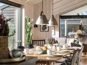A dining area with a wooden table set for breakfast, featuring white cups, plates, and a basket of bread.