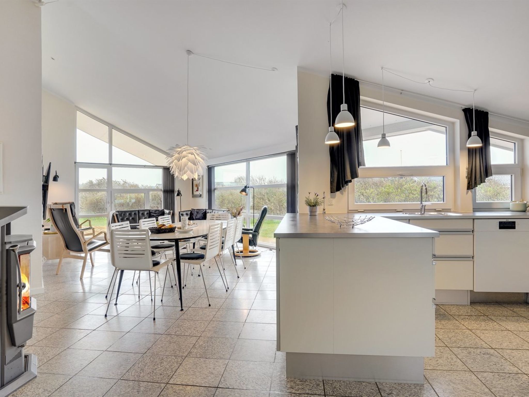 Une cuisine moderne dotée d’un îlot central, de grandes fenêtres et d’un coin repas avec des chaises et une table.