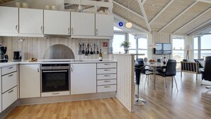 Een moderne keuken met witte kastjes, een inbouwoven en een eethoek met een tafel en stoelen.