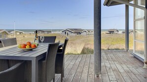 Een houten terras met een tafel gedekt voor twee, met uitzicht op een strand met strandhuisjes.