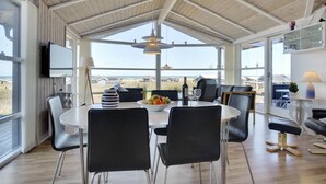 Een ruime eethoek met een hoge plafond en grote ramen met uitzicht op het strand.