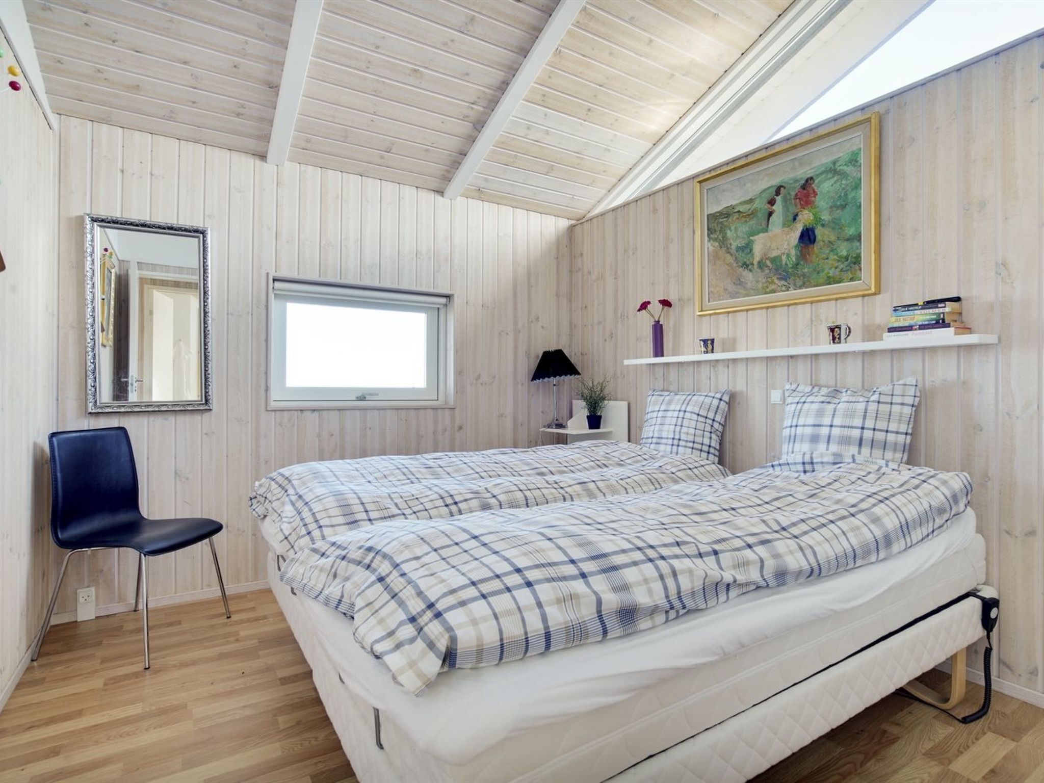 Ein Schlafzimmer mit einem Bett, einem Sessel, einem Fenster, einem Spiegel und einem Bild an der Wand.