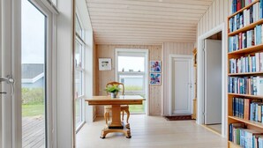 Een hal met een houten vloer, een tafel met een plant en een boekenkast vol boeken.