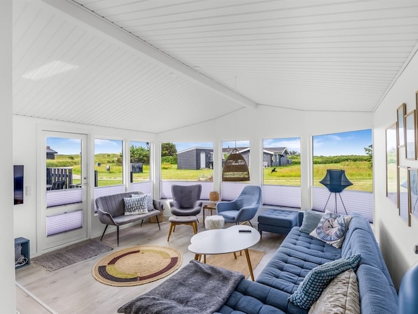 A sunlit room with a blue sofa, two chairs, a small table, and a large window offering a view of the outdoors.