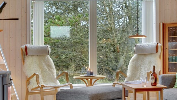 A cozy room with a large window, two plush chairs, a grey sofa, a wooden table, and a hanging light fixture.