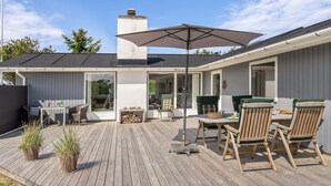A wooden deck with a table and chairs, a large umbrella, and a chimney.