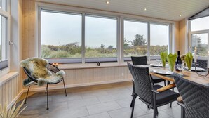 A dining area with a view of the landscape through large windows, wooden paneling, and wicker chairs.