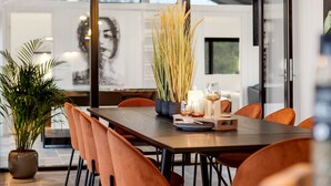 A modern dining area with a long table, orange chairs, and a potted plant.