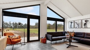 A modern living room with a large sliding glass door leading to a grassy outdoor area, a sofa, a coffee table, and a chair.