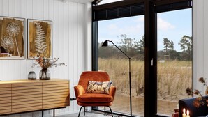 A modern living room with a large window, a wooden sideboard, an orange armchair, and a floor lamp.