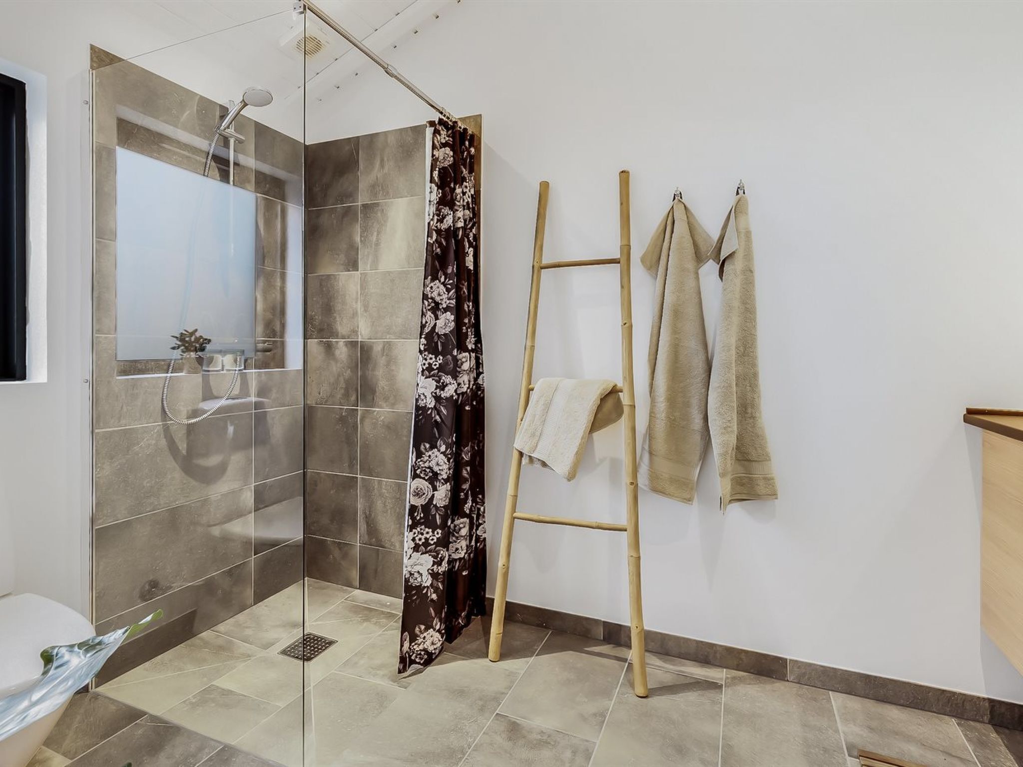 Une salle de bain moderne avec une douche à parois de verre, un escabeau en bambou et des serviettes accrochées au mur.