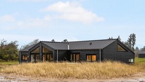 A modern two-story house with a dark exterior, large windows, and a sloped roof.