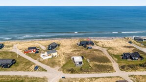 An aerial view of a coastal property with multiple houses, a beach, and a clear view of the ocean.