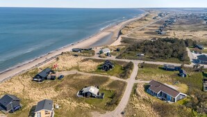 An aerial view of a coastal area with a beach, houses, and a road.