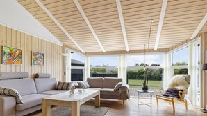 A spacious living room with a wooden ceiling, large windows, and a view of the outdoors.
