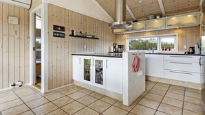 A modern kitchen with wooden walls, a central island, white cabinets, and a large window overlooking greenery.
