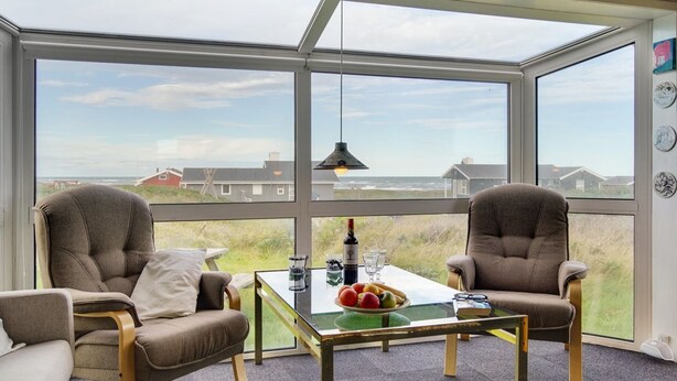A room with two chairs, a glass table, and a view of the beach and houses.