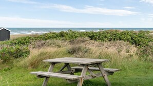 A wooden picnic table in a grassy area with a view of the ocean and a beach in the background.