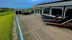 Une terrasse avec une table et des chaises, donnant sur une pelouse et un bâtiment doté de grandes fenêtres.