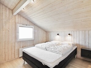 Un dormitorio con techo de madera, una ventana, una cama con ropa blanca y un televisor pequeño sobre un pedestal.