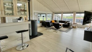Un vaste espace de vie doté d’un haut plafond, d’un canapé noir, d’une table à manger et d’un coin cuisine avec des placards en verre.