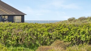 Une maison située sur la côte, avec un toit en métal, entourée d’une végétation luxuriante et offrant une vue sur la mer.