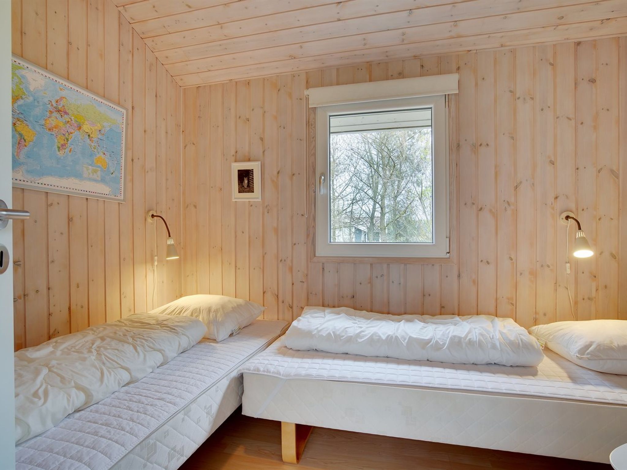 Ein Zimmer mit Holzwänden, zwei Betten, einem Fenster, einer Karte an der Wand und einem Bild.