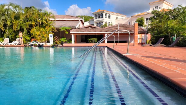 En pool med klart, blått vatten och avgränsade banor, omgiven av solstolar och palmer.