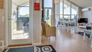 Une pièce spacieuse dotée d’une grande porte-fenêtre coulissante donnant sur un espace extérieur, d’une table à manger avec des chaises, d’un fauteuil en osier, d’un téléviseur et d’un ventilateur de plafond.