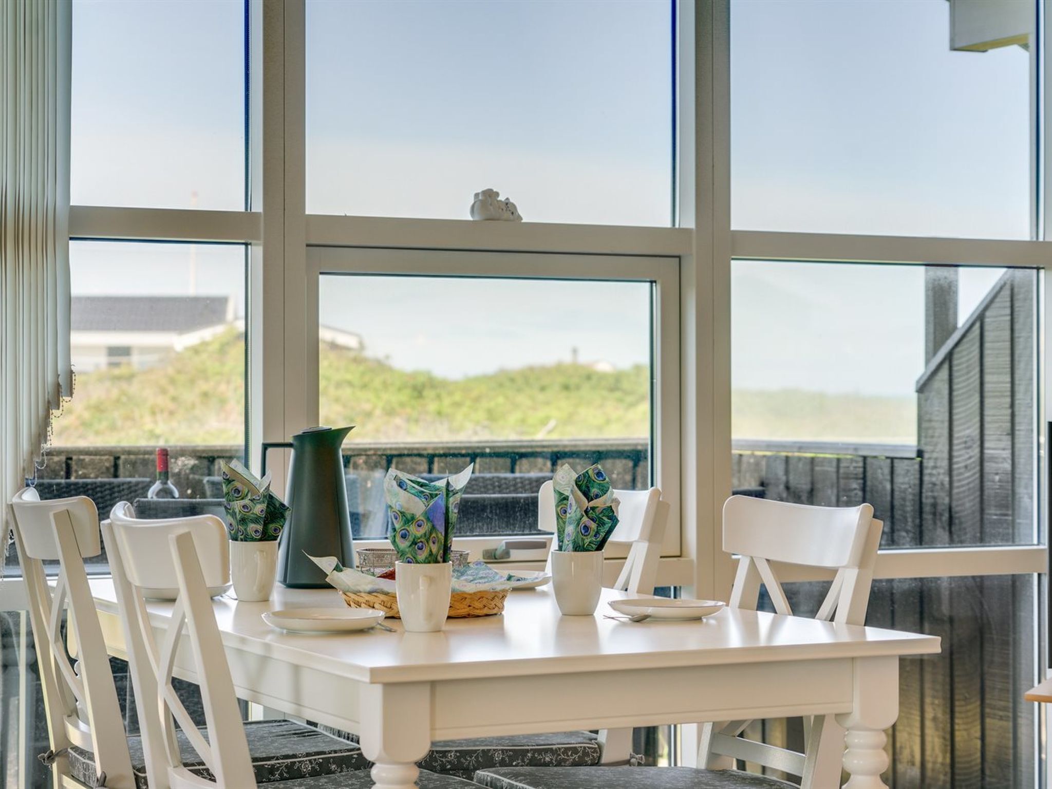 Une table à manger avec des chaises, un vase et des objets décoratifs sur un balcon donnant sur la plage.