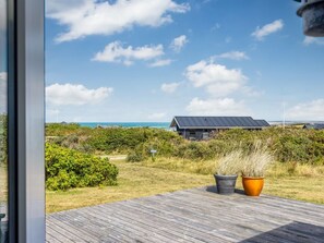 A wooden deck with potted plants, overlooking a beach with a house and vegetation. - "Marjanna" - 350m from the sea by Interhome (Hjørring)