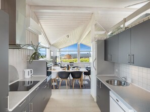 A modern kitchen with a dining area, large windows, and a view of the outdoors.