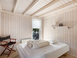 Ein Schlafzimmer mit einem Bett, einem Stuhl, einem Fenster und einem Regal mit Flaschen.