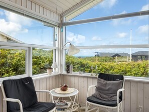 A sunroom with two wicker chairs, a small table, and a view of the countryside.