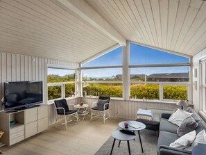 A sunlit room with a TV, seating, and a view of greenery and buildings. - "Marjanna" - 350m from the sea by Interhome (Hjørring)