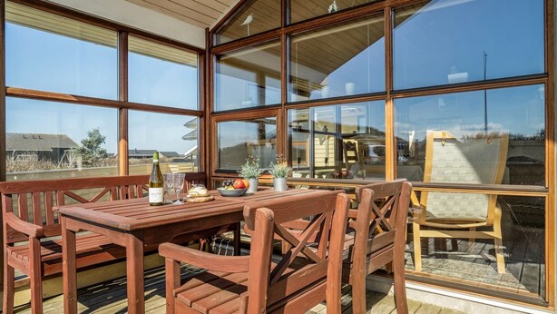 Une terrasse en bois avec une table et des chaises, de grandes fenêtres et une vue sur le paysage.
