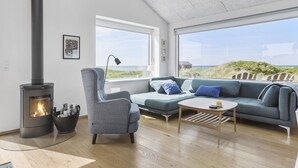 Ein modernes Wohnzimmer mit Kaminofen, einem grauen Sessel, einem blauen Sofa und einem Holztisch.