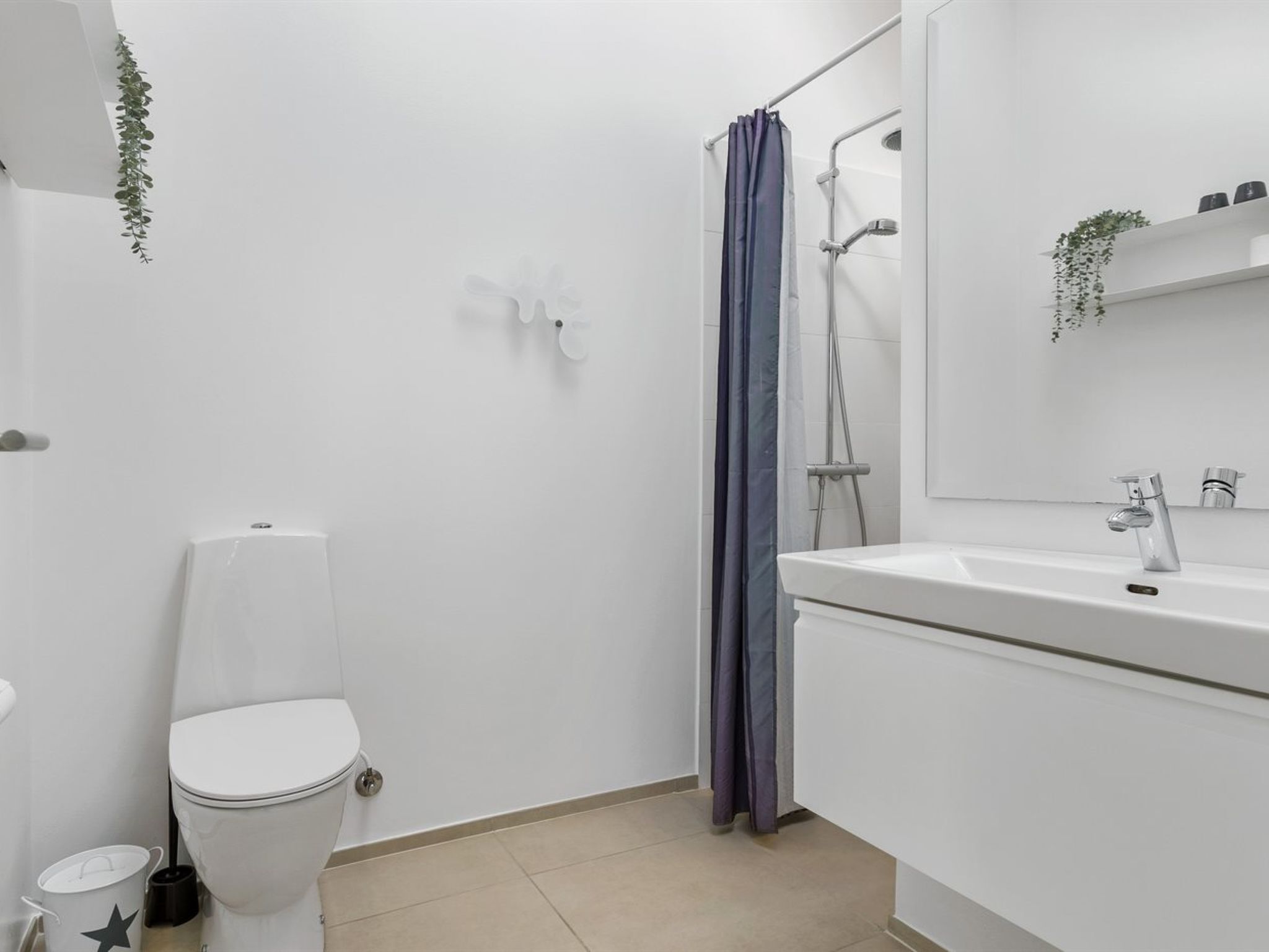 A compact, modern bathroom with a white toilet, a shower with a blue curtain, and a white sink with a mirror above it.