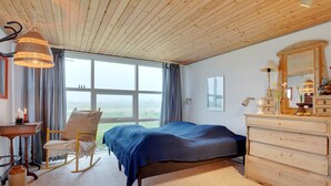 A bedroom with a wooden ceiling, a large window with a view, a bed, a dresser, a chair, and a desk with a lamp. - "Stavros" - 410m from the sea by Interhome (Hjørring)