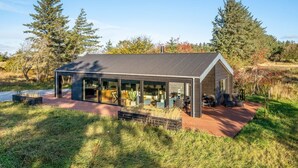 Una casa moderna amb un ampli envàs de vidre, envoltada d'un paisatge natural.
