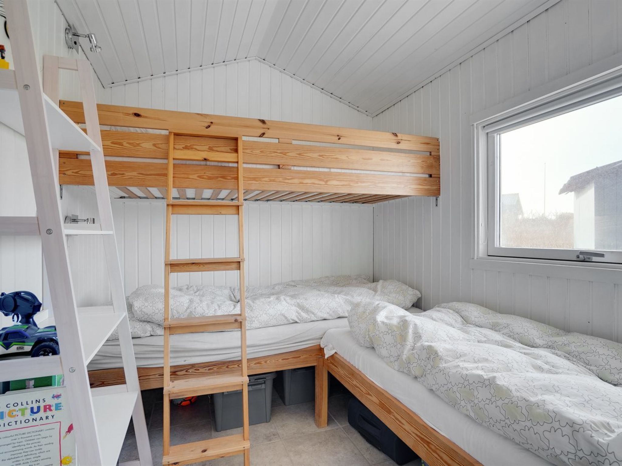 A bunk bed room with a ladder, a window, and a shelf with a book.