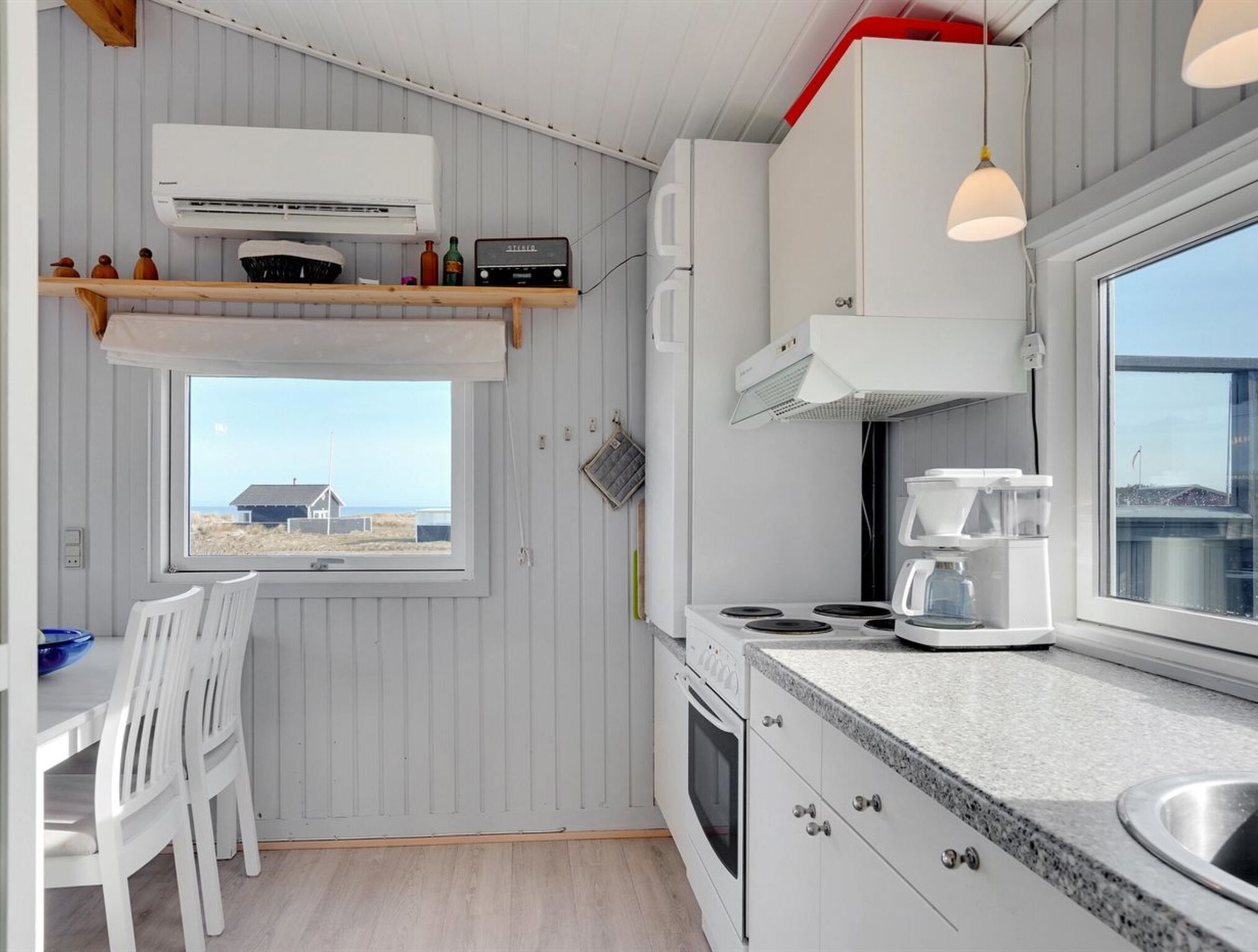 A compact kitchen with a window, white cabinetry, a stove, and a sink.
