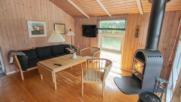A cozy cabin interior with a wooden floor, a sofa, a dining table, chairs, a fireplace, and a TV mounted on the wall. - "Nakke" - 1.3km from the sea by Interhome (Hjørring)