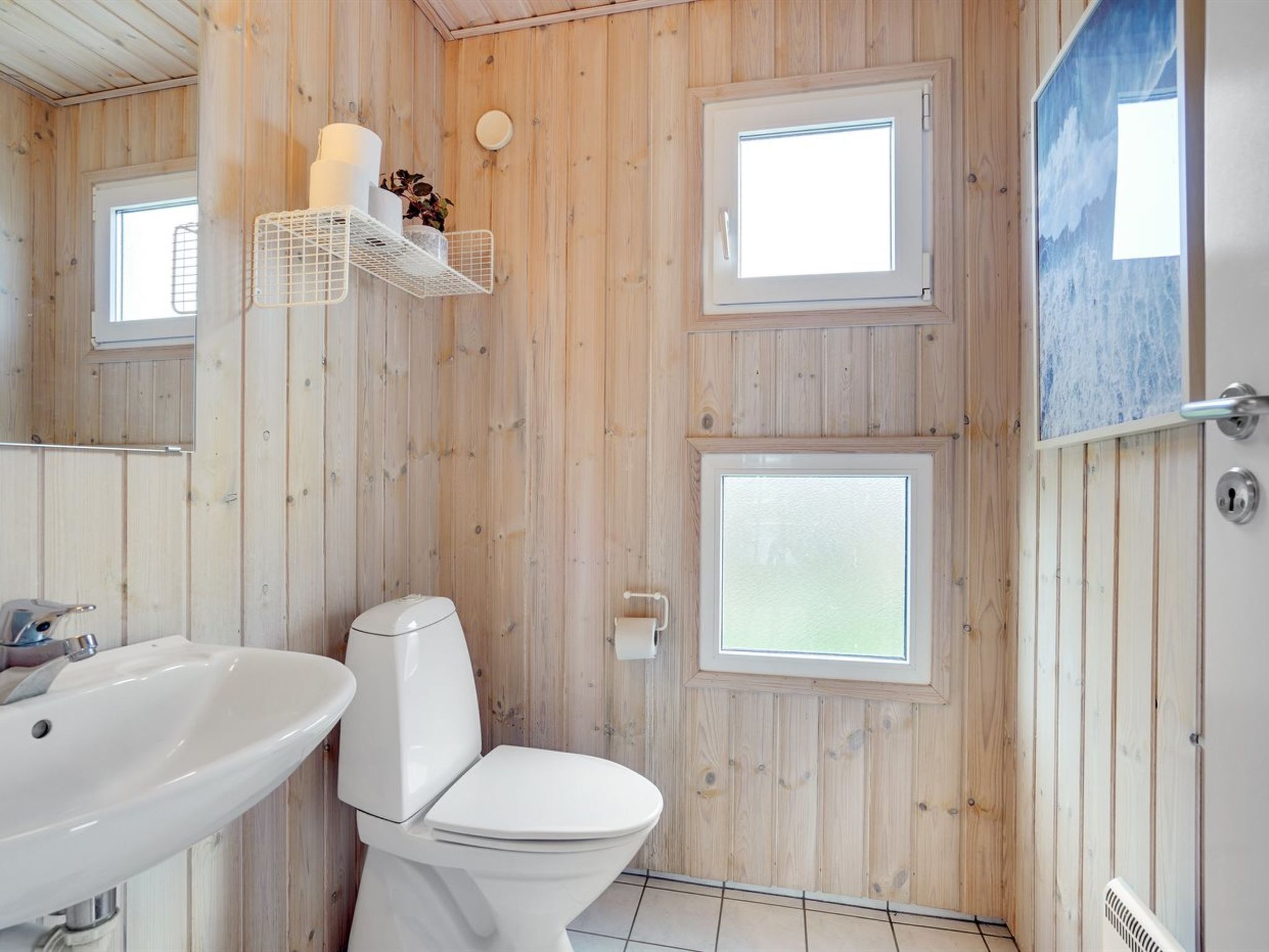 Een badkamer met houten wanden, een wit toilet, een wastafel en twee ramen.