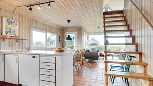 Una cocina espaciosa con una isla central, una escalera de madera y ventanas amplias que ofrecen vistas al exterior.