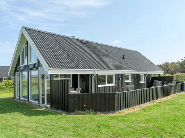 A modern house with a large glass window, a covered patio with outdoor furniture, and a metal roof.